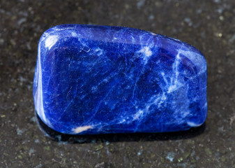closeup of sample of natural mineral from geological collection - tumbled Sodalite rock on black granite background from Brazil