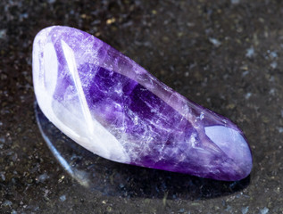 closeup of sample of natural mineral from geological collection - rolled Amethyst rock on black granite background from Namibia