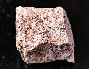closeup of sample of natural mineral from geological collection - unpolished Aplite rock on black granite background