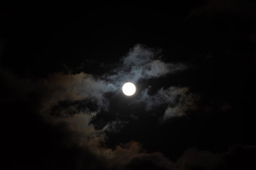 Naklejka na ściany i meble A full moon with clouds in the black night sky. Full moon on January 31, 2018. A supermoon. Beautiful clouds in the night sky. Natural mysterious background. Space. Bright light from the moon
