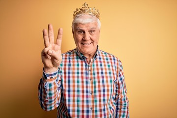 Naklejka premium Senior handsome hoary man wearing golden crown of king over isolated yellow background showing and pointing up with fingers number three while smiling confident and happy.