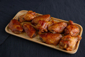 Baked chicken wings in a wooden dish on a dark cloth.