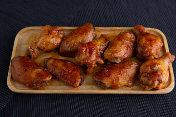 Baked chicken wings in a wooden dish on a dark cloth.