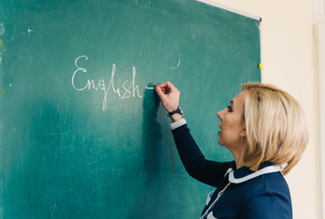 Young female teacher holding a chalk and writing on the blackboard. Educational process.