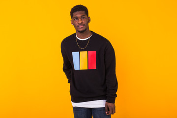Handsome African American man posing in black sweatshirt on a yellow background. Youth street...