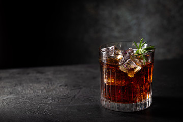 Glass of cold cola with ice cubes on dark background