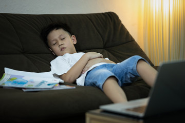 Online education for kindergarteners, kid boy student is sleeping on the sofa while studying online,learning online with laptop computer at home during the pandemic of Coronavirus Covid-19,stay home