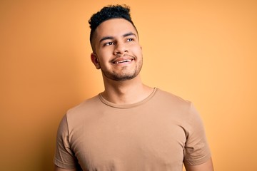 Young handsome man wearing casual t-shirt standing over isolated yellow background looking away to side with smile on face, natural expression. Laughing confident.
