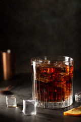 Glass of cold cola with ice cubes on dark background