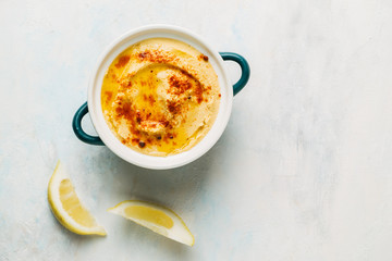 dish of hummus with olive oil and paprika. Next to it are some lemon slices. Image seen from above. Food concept