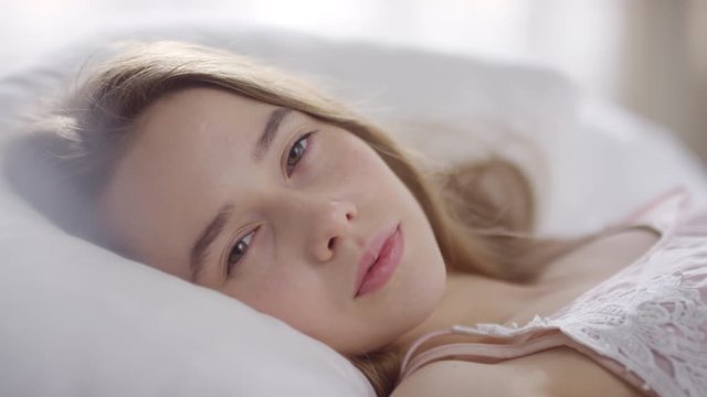  Close up of serene young woman sleeping in bed on peaceful morning, then waking up and looking at camera
