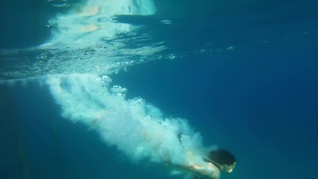 Slow-motion shot of a young woman diving from a wooden pier to a clear blue sea. Underwater shot.