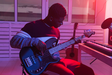 Obraz premium Create music and a recording studio concept - African american man guitarist recording electric bass guitar track in home studio