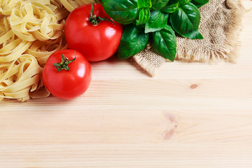 Basil leaves, tomatoes and raw pasta on wooden background.