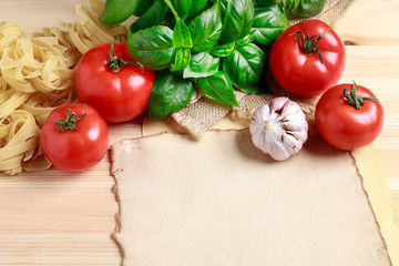 Basil leaves, tomatoes and raw pasta on wooden background.