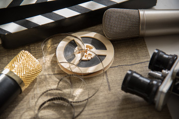 Fototapeta premium Film reel, movie clapperboard, two microphones and an old movie camera with two lenses on a table with a gray
