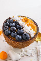 smoothie bowl with mango, blueberry and coconut shavings in coconut bowls on white background, mango sherbet
