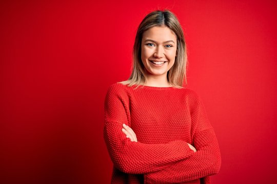 Young beautiful blonde woman wearing casual sweater over red isolated background happy face smiling with crossed arms looking at the camera. Positive person.