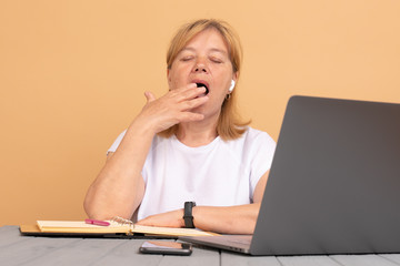 Middle age senior woman sitting at the table at home working using computer laptop bored yawning tired covering mouth with hand.