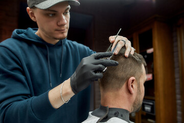 Hairstylist working at barbershop. Young barber in cap making haircut for his client in barber shop. Mens haircut