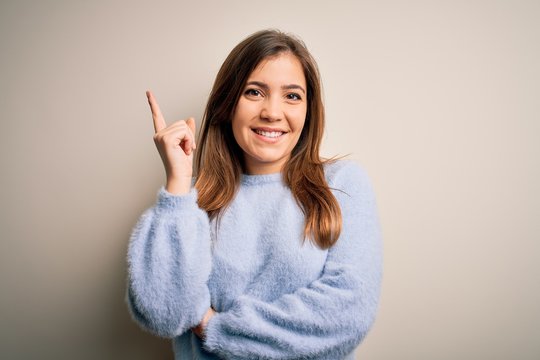 Beautiful young woman wearing casual winter sweater standing over isolated background with a big smile on face, pointing with hand and finger to the side looking at the camera.