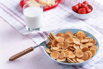 mini cereal pancakes in blue bowl with fork, strawberries, glass of milk on white background, rural Breakfast concept