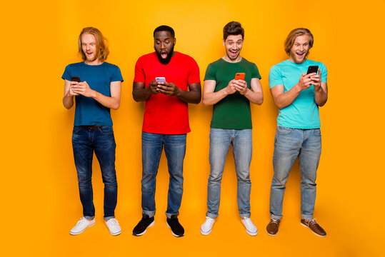 Full length photo of excited surprised four men people use cellphone impressed social network subscribe report wear t-shirt denim jeans isolated over bright shine color background