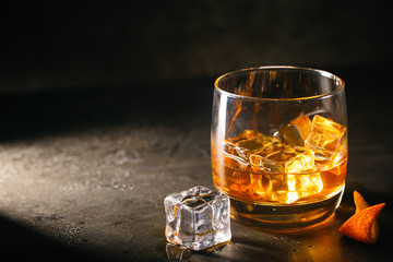 Glass of scotch whiskey with ice cubes on black background