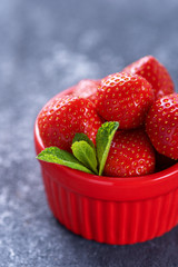 closeup summer strawberries in red bowl with mint on gray background, strawberry harvest