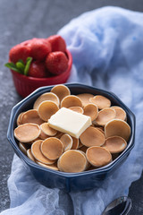 trendy cereal pancakes in blue bowl with buttering toast and strawberry on blue gauze on grey background