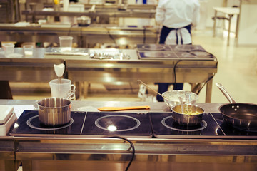 Pans stand on the stove in a large kitchen with the chefs of a restaurant or cafe