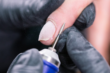 Hardware manicure in a beauty salon. Female manicurist is applying electric nail file drill to manicure on female fingers. Mechanical manicure close-up. Concept body care.