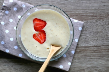 Bowl of vegan banana nice cream with strawberry toppings, polka dot napkin and wooden spoon. Top view.
