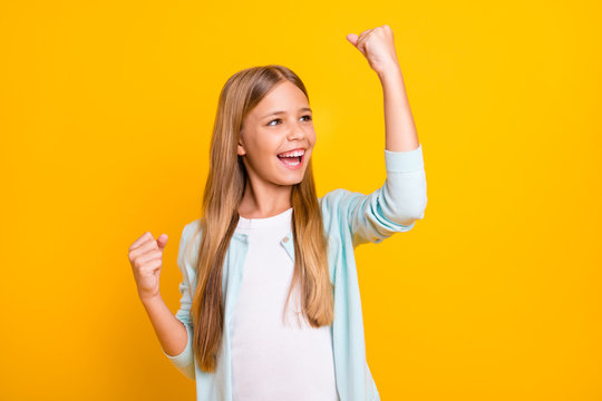 Photo of beautiful funny little blond lady good mood celebrate best holidays beginning raise fists excited open mouth wear casual blue shirt isolated yellow color background