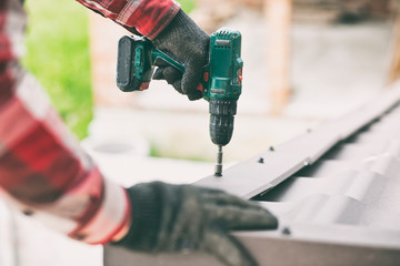 The roofer worker screwing the metal tile on the roof