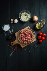 Raw minced meat with ingredients on black wooden boards