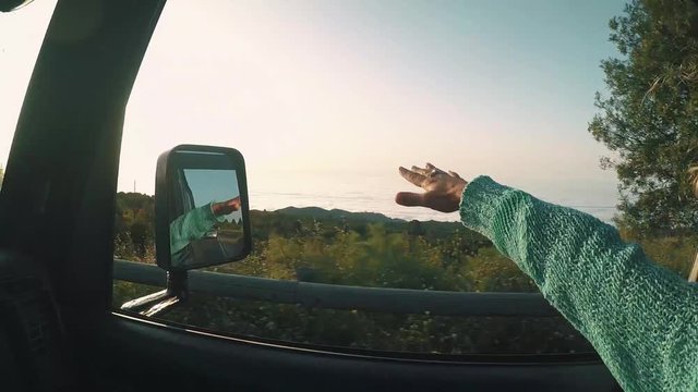 Adult happy and free traveler woman play with the wind travel on car vehicle on the road and colorful sunset view outside the window - concept of summer holiday trip vacation life