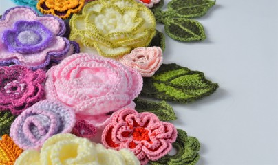 Multicolored crocheted flowers and leaves close up on a white background with copy space. 