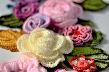 Multicolored crocheted flowers and leaves on white background close up.