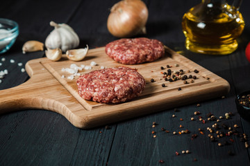 Cutlets from minced meat with the ingredients on the black wooden table.