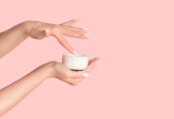 Poster Unrecognizable girl applying cream from jar onto her hands against pink background, blank space © Prostock-studio