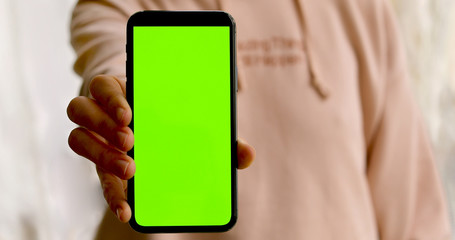 Woman shows a smartphone with a green screen. Person has reached out a hand and is showing a blank screen mockup
