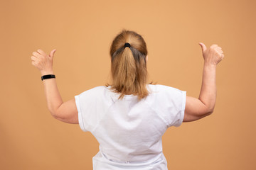 Female in white blank t-shirt standing back to the camera with raised hands, holding thumbs up