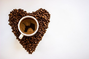 White coffee cup and beans hart shape background.Heart with fresh roasted coffee beans on a white background.Coffee love in early morning time.Heart shape made from coffee beans on wooden background