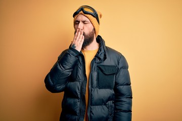 Handsome skier bald man with beard skiing wearing snow sportswear and ski goggles bored yawning tired covering mouth with hand. Restless and sleepiness.