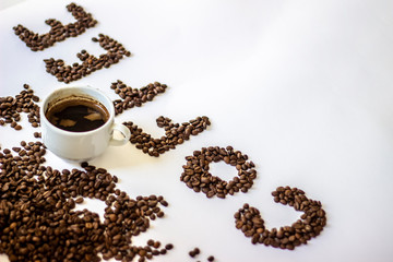Cup of black coffee on white background with letter coffee wrote from fresh rosted beans. White cup of coffee and letters Coffee. Brown coffee letters isolated on a white background. Copy-space.