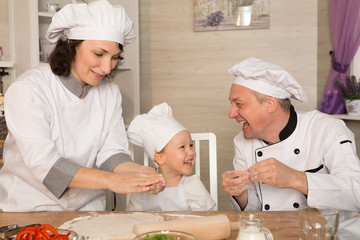 Mom, dad and little son cook together in quarantine. The family laughs and cooks pizza in cookery suits.