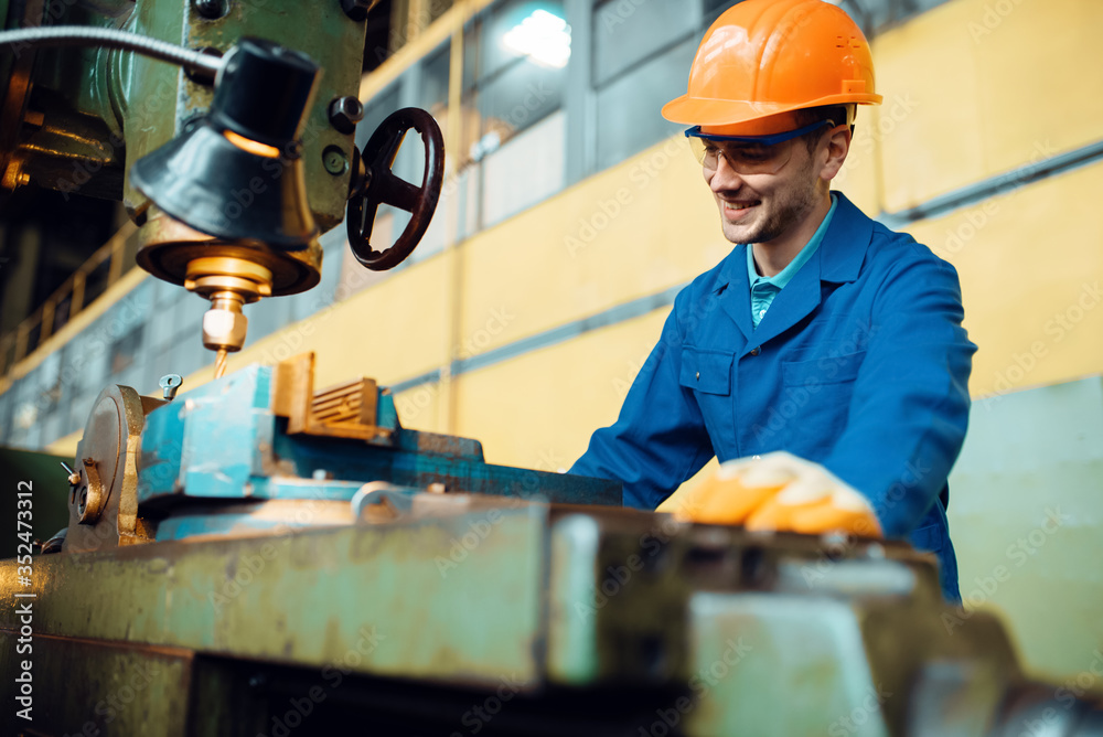 Wall mural Turner in uniform and helmet works on lathe, plant