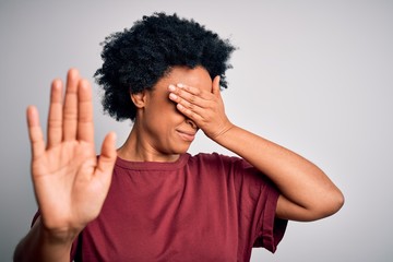 Fototapeta na wymiar Young beautiful African American afro woman with curly hair wearing casual t-shirt standing covering eyes with hands and doing stop gesture with sad and fear expression. Embarrassed and negative