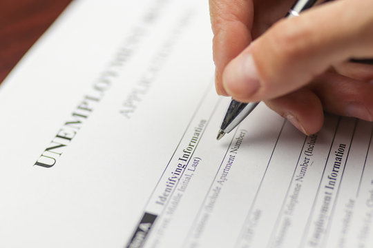 Close-up of a person's hand filing social security benefits application form.  Concept of Covid-19 coronavirus and stay at home order impact on economy, world economic crisis, unemployment.